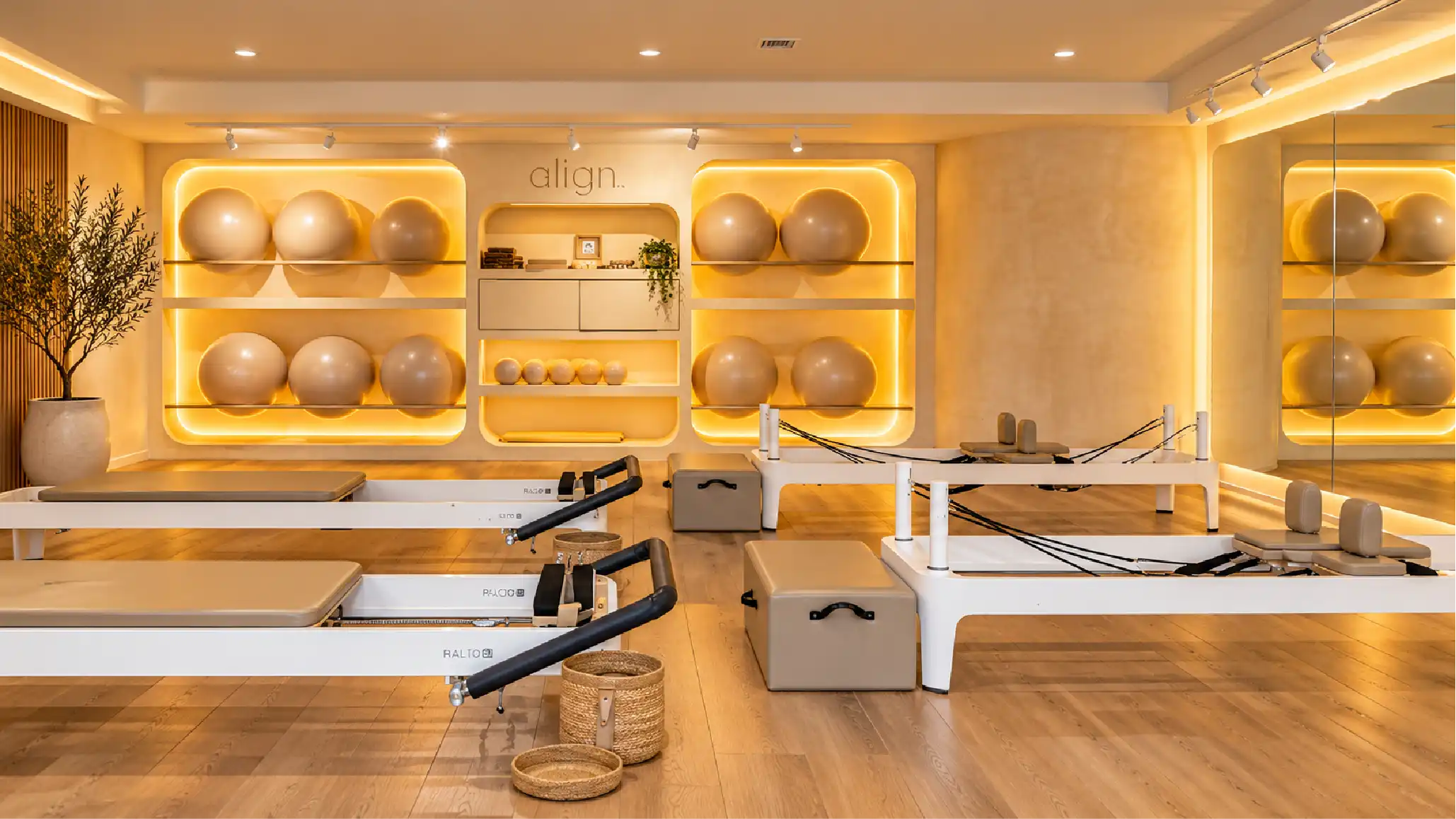 Align Pilates Reformer — acabados arquitectónicos de estudio de pilates en Querétaro Estudio Align Pilates Reformer en Querétaro con camas reformer, nichos iluminados para pelotas, piso de madera y muro de chukum