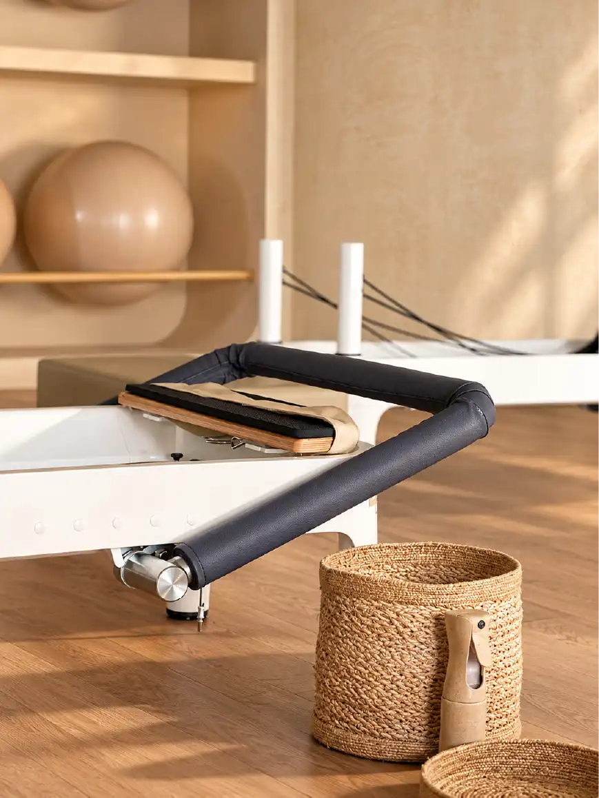 Detalle de cama reformer con barra acolchada y cesto de fibra natural sobre piso de madera en el estudio Align Pilates Reformer en Querétaro