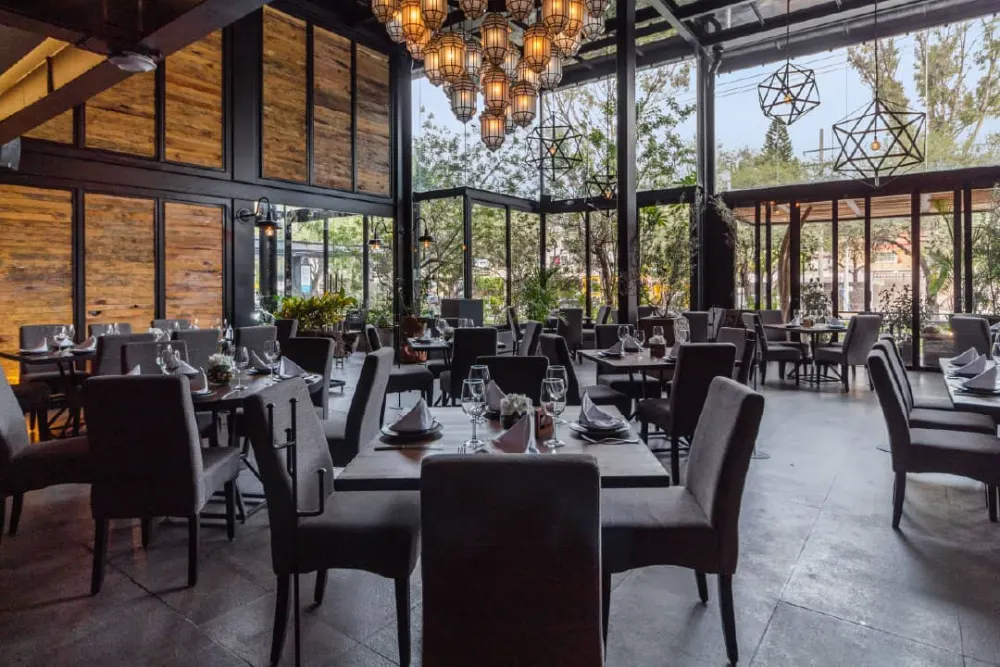 Comedor con ventanales de doble altura y candil de lámparas colgantes en la construcción del restaurante Don Vito