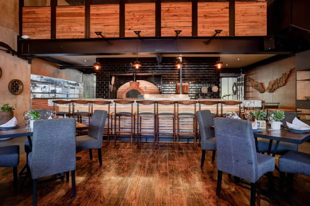 Barra de madera frente al horno italiano y muro de ladrillo negro, diseño de interiores del restaurante Don Vito