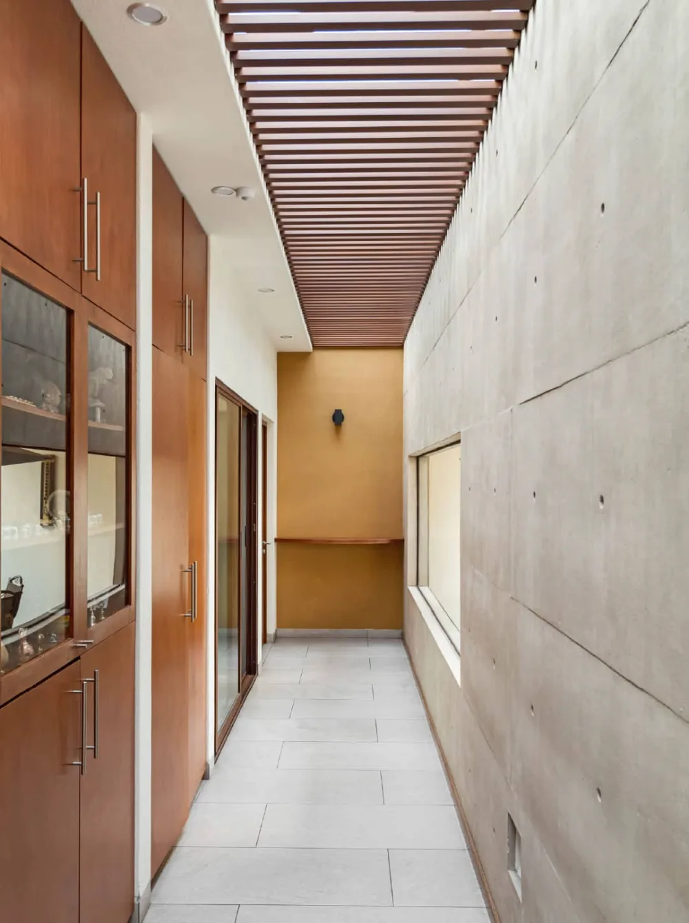Pasillo interior de Casa CAED con muro de concreto aparente y techo de madera, Corregidora, Querétaro