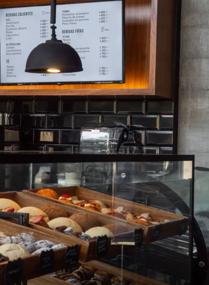 Vitrina con panes artesanales y pantalla de menú de bebidas en la panadería Pan de Lucio en Querétaro