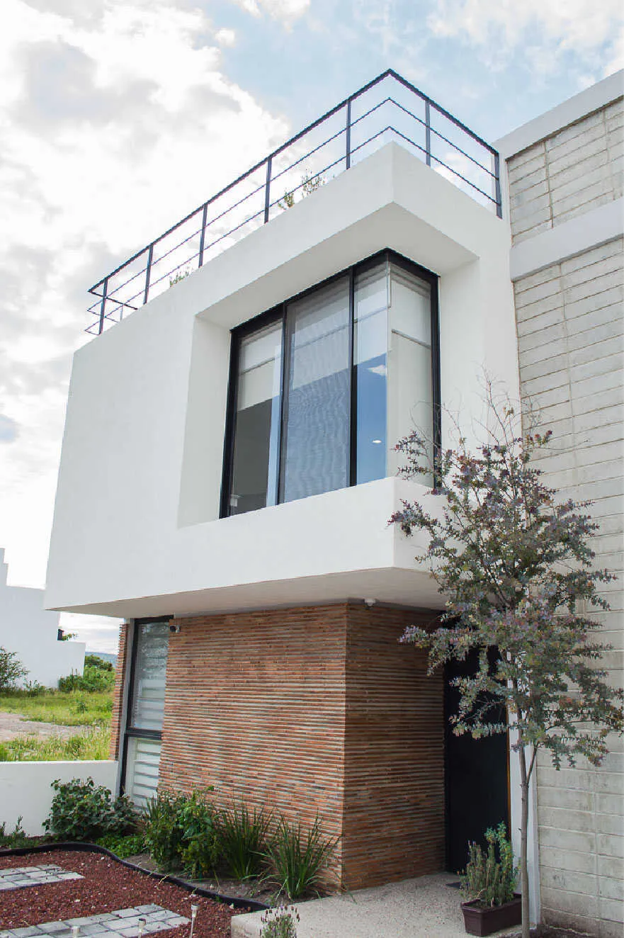 Fachada de Casa Moro con volumen blanco y muro de ladrillo en Biogrand Juriquilla, Querétaro