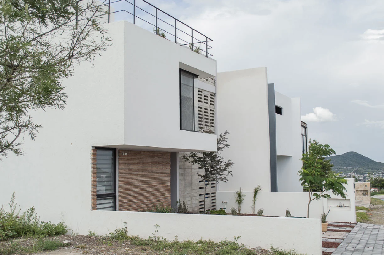 Vista lateral de Casa Moro con muros blancos, ladrillo y celosía de concreto en Biogrand Juriquilla