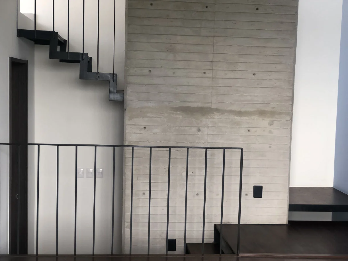 Medios niveles con barandal metálico y escalera junto a muro de concreto aparente en Casa Moro, Biogrand Juriquilla
