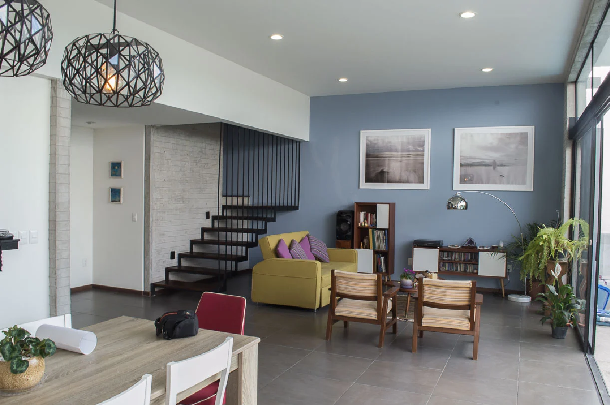 Sala y comedor de planta abierta con escalera volada y muro azul en Casa Moro, Querétaro