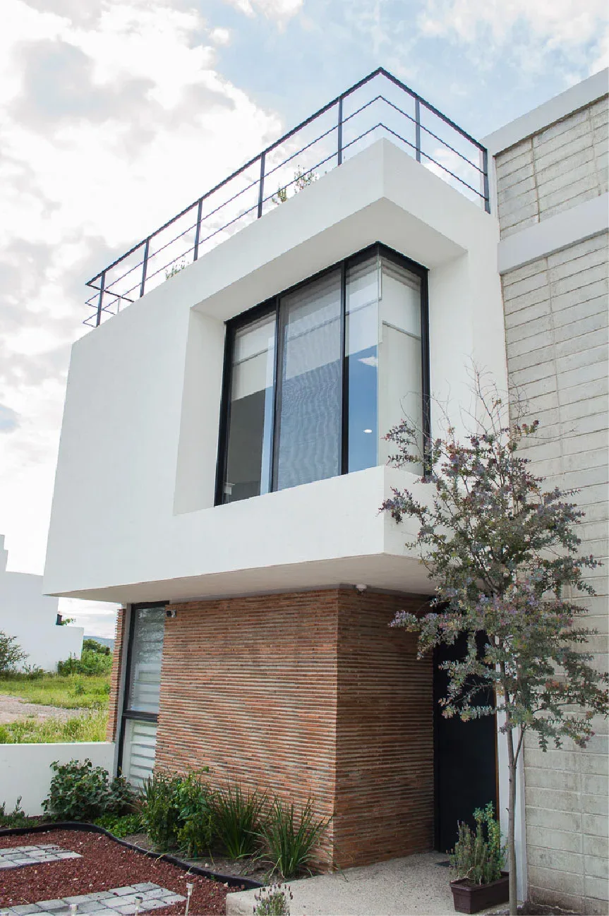 Volumen blanco en voladizo con ventanal y muro de ladrillo aparente de Casa Moro en Biogrand Juriquilla, Querétaro