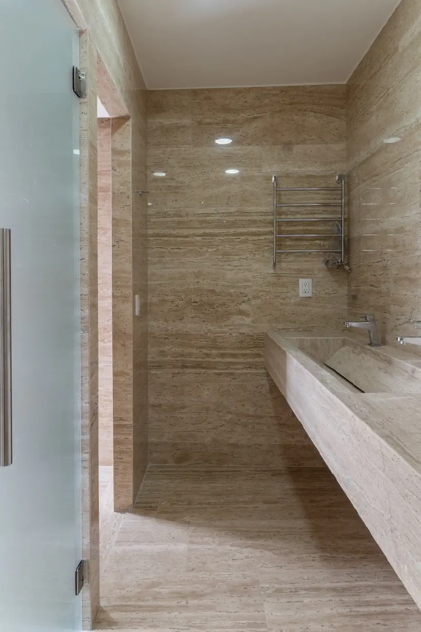 Baño revestido en travertino con lavabo tallado y toallero eléctrico en Casa Paseo, Juriquilla