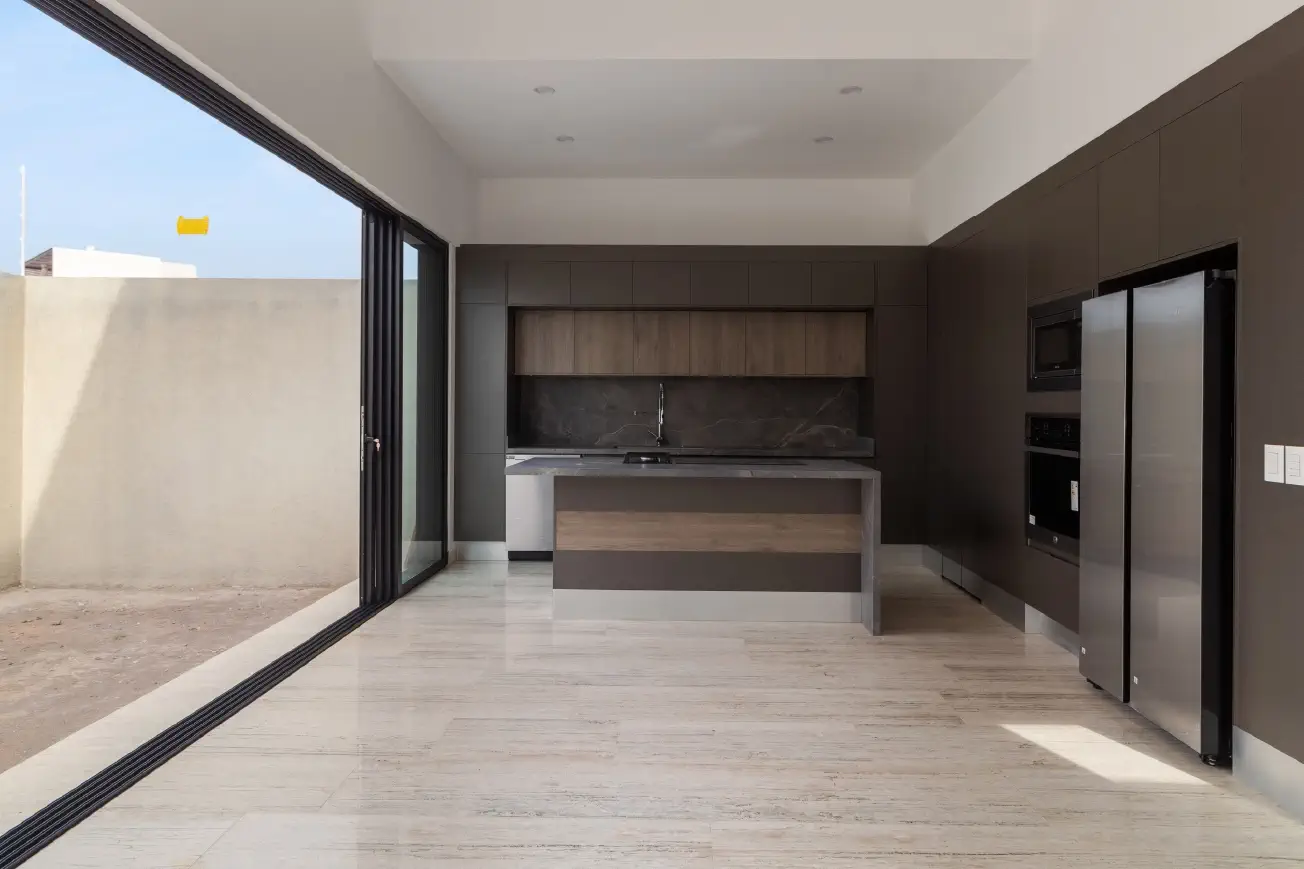 Cocina con isla, gabinetes oscuros y puerta corrediza de piso a techo hacia el patio en Casa Paseo