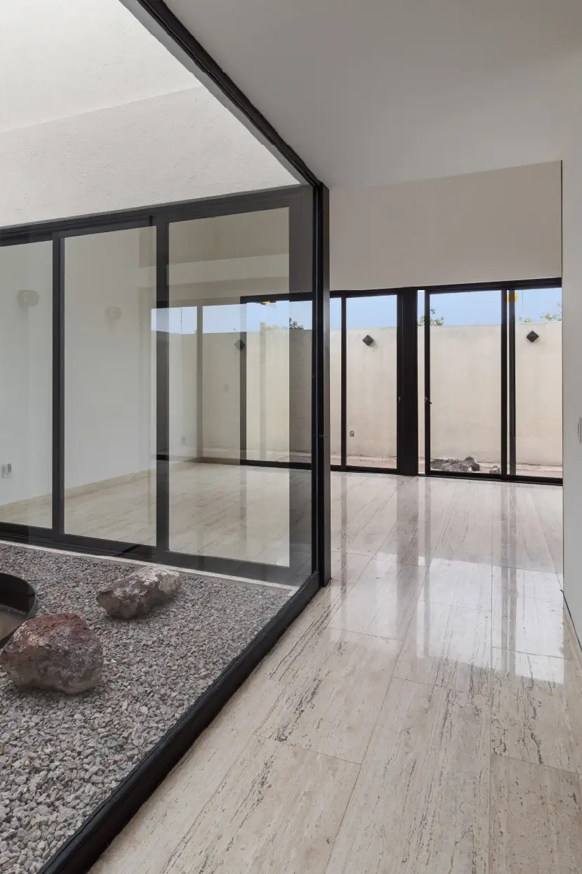 Patio interior con grava y rocas volcánicas visto a través de cancelería negra en Casa Paseo
