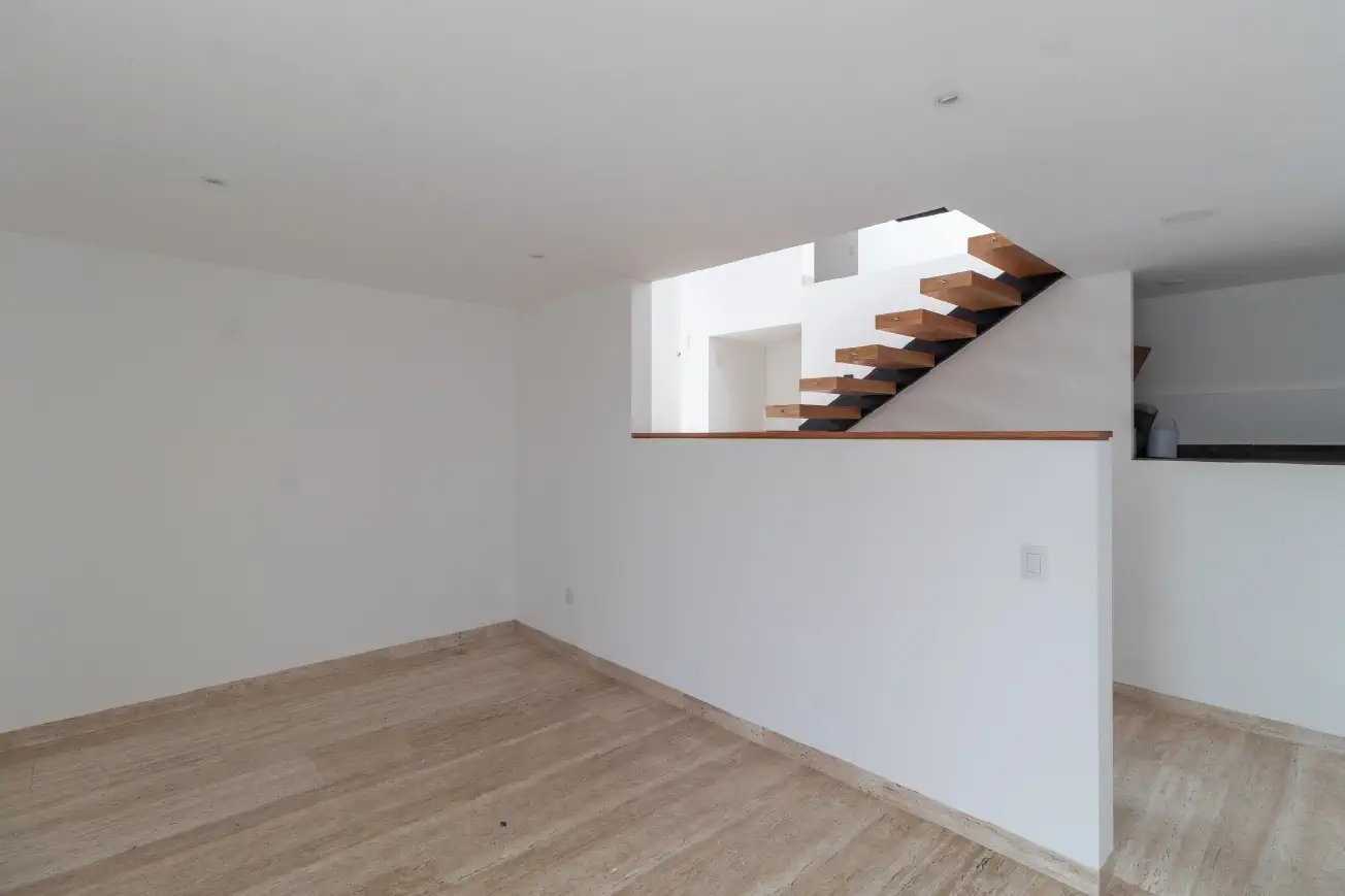 Sala con escalera flotante de madera y muro en medio nivel en Casa Paseo, Juriquilla