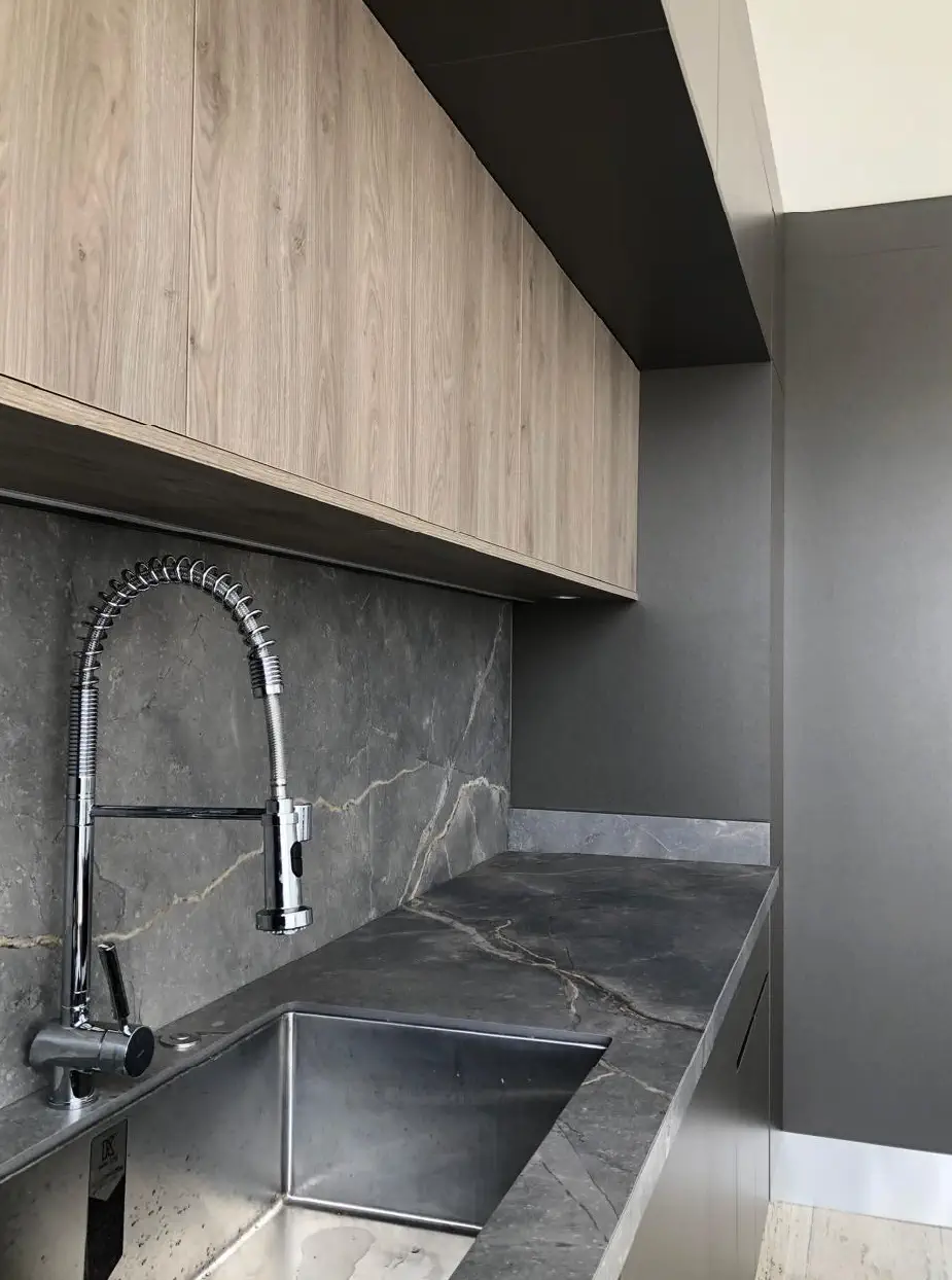 Tarja de acero, cubierta y salpicadero de piedra con gabinetes de madera en la cocina de Casa Paseo