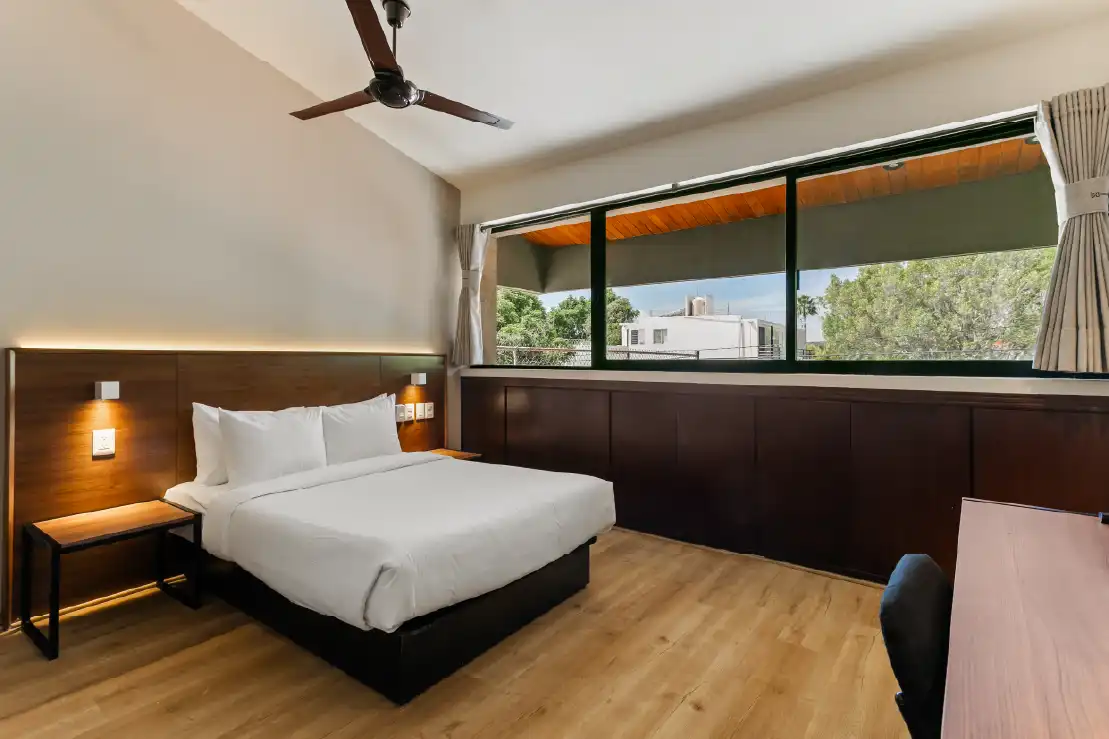 Habitación de renta vacacional con cama, cabecera de madera y ventanal hacia el jardín en Querétaro