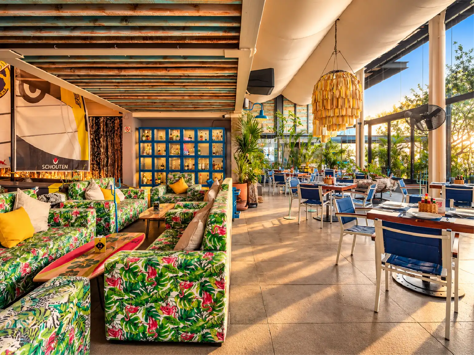 Sala lounge con sofás de estampado tropical y ventanales al jardín en el espacio gastronómico Yellow Fish