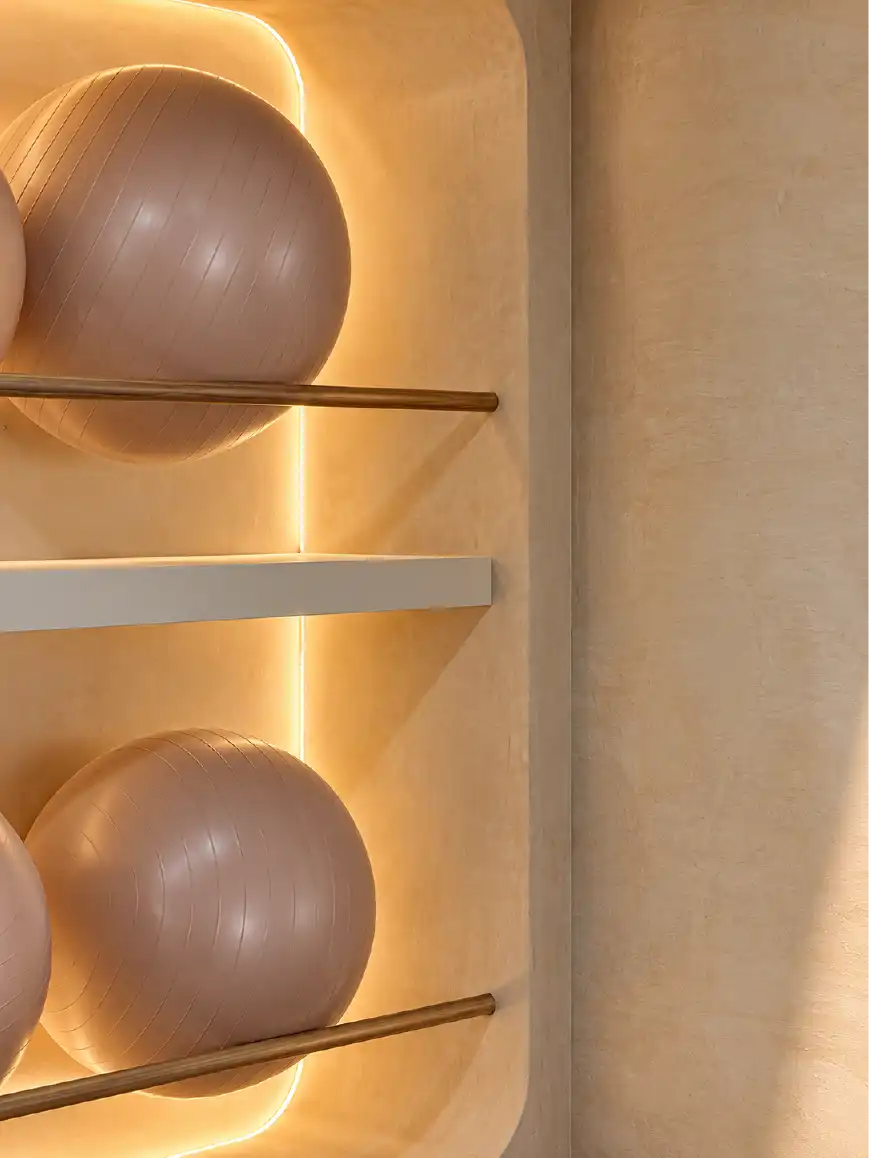 Detalle de iluminación led en nicho de madera con pelotas de pilates y muro texturizado de chukum