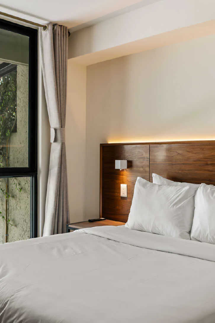 Cabecera de madera con luz indirecta y cortina de lino en habitación Homi Rent para Airbnb en Querétaro