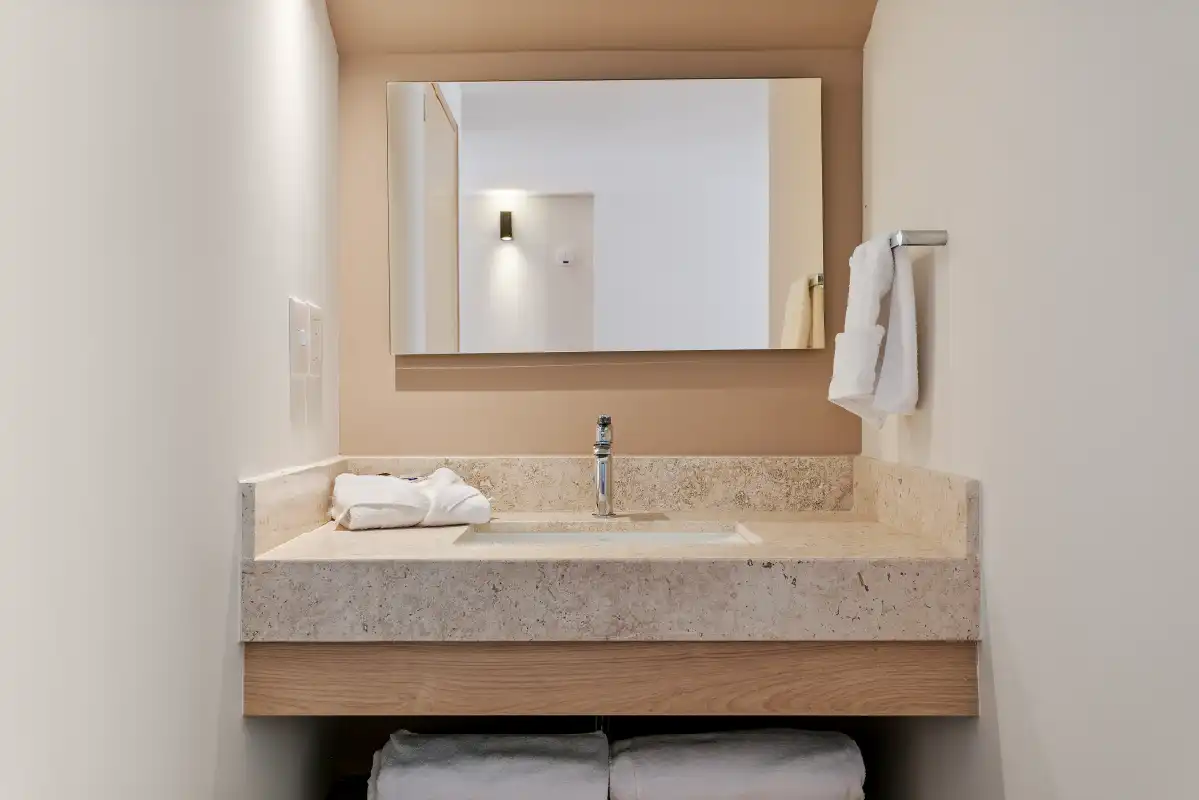 Lavabo de cantera con espejo rectangular y gabinete de madera en baño de renta vacacional