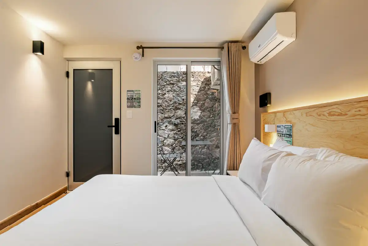 Recámara con puerta, ventanal a muro de piedra y cabecera de madera en casa remodelada para renta