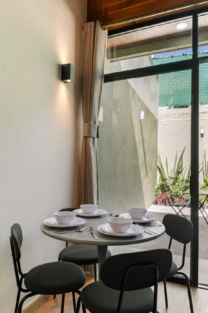 Comedor redondo con sillas negras junto a ventanal y patio en departamento de inversión en Querétaro