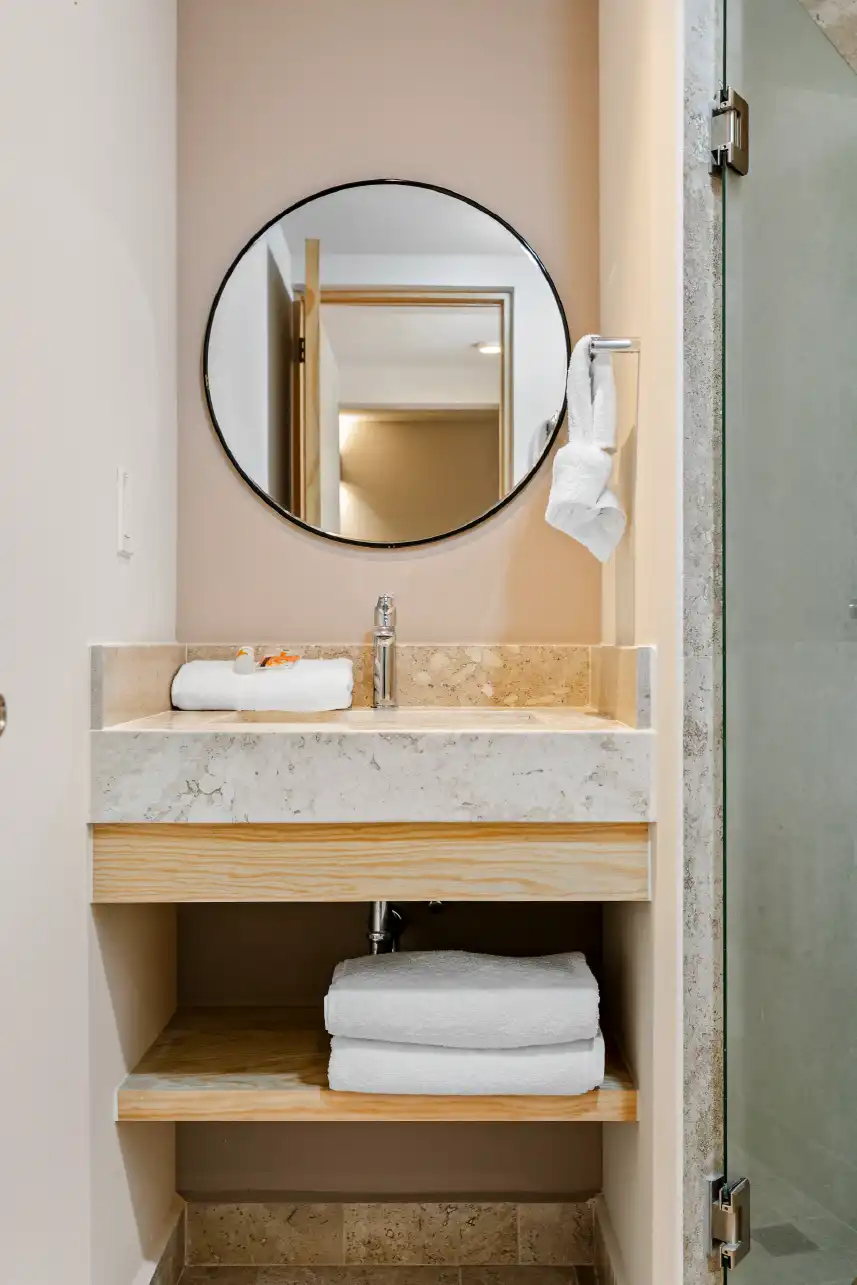 Lavabo con espejo circular y repisa de madera en baño de inversión en Querétaro