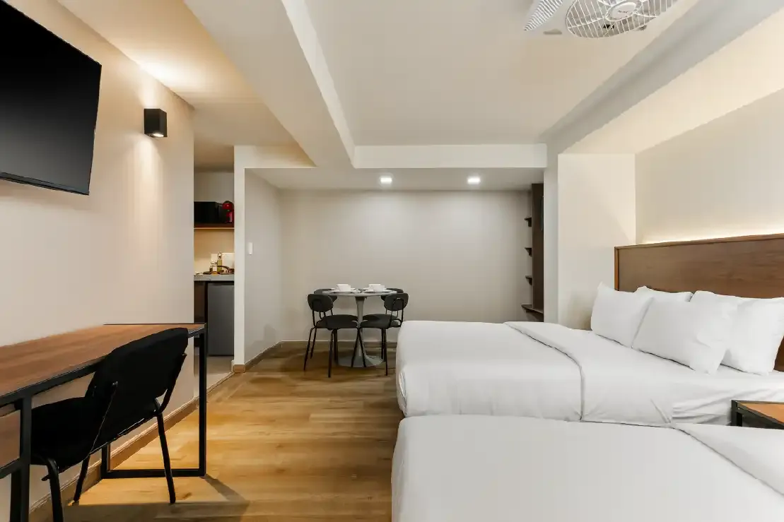 Estudio con dos camas, escritorio y cocineta al fondo en inversión inmobiliaria para Airbnb en Querétaro