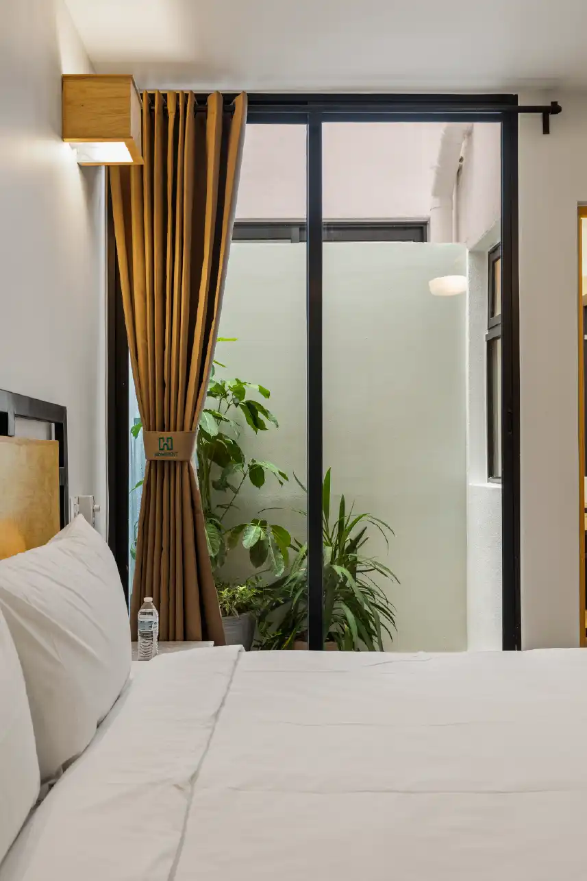 Recámara con cortina ocre, ventanal y patio con plantas en departamento de inversión en Querétaro