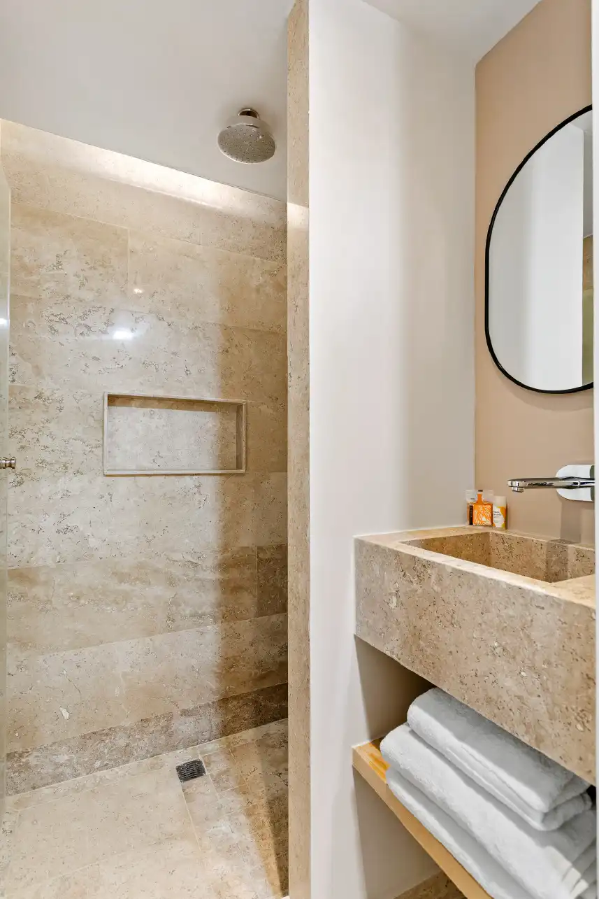 Baño con regadera de piedra y lavabo tallado en departamento de inversión en Querétaro