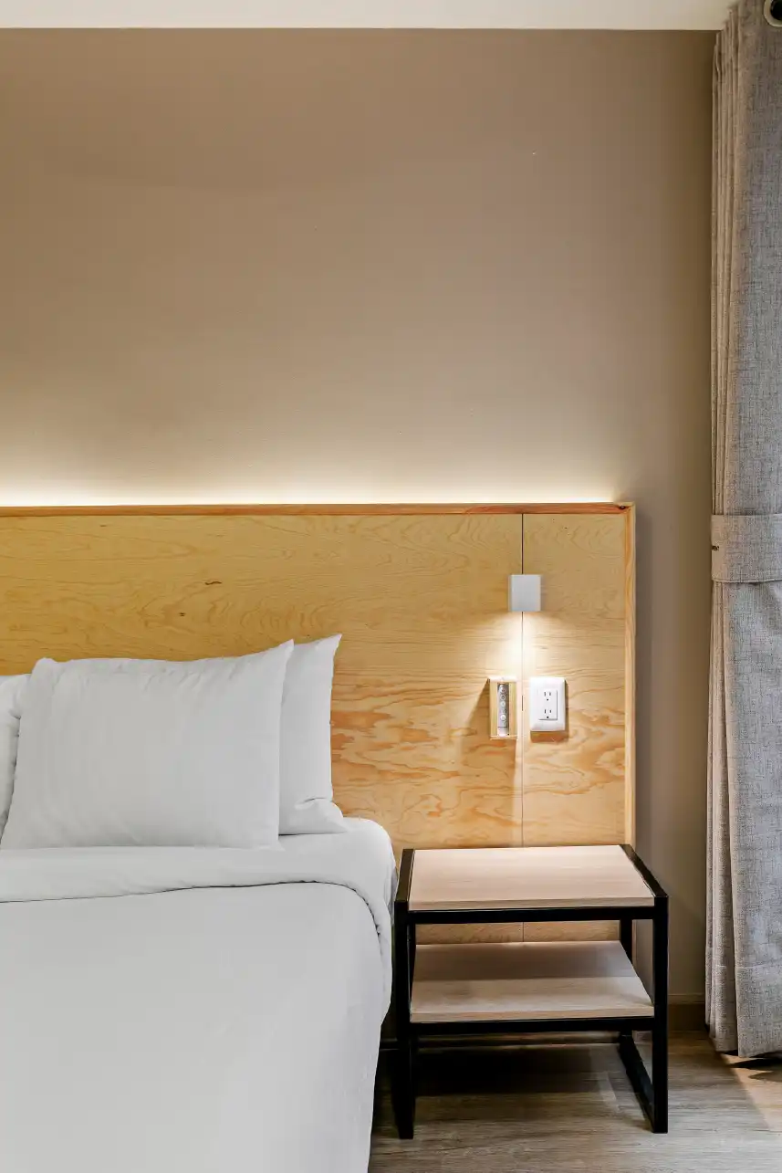 Cabecera de madera con luz indirecta y buró metálico en habitación para renta en Querétaro