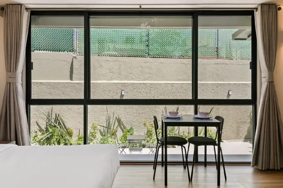 Ventanal de piso a techo con cortinas y comedor frente a patio con plantas en propiedad Homi Rent en Querétaro