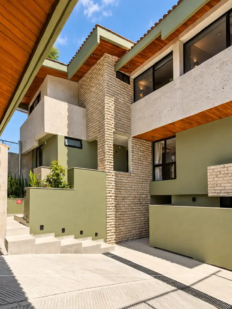 Proyecto de inversión Hierba, Querétaro Fachada de complejo de suites con cantera, ladrillo, plafón de madera y muros verdes en Querétaro