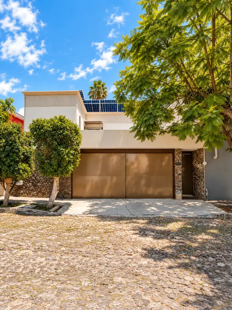 Proyecto de inversión Olmo, Querétaro Fachada de casa remodelada para renta vacacional con portón cobrizo, muro de piedra y paneles solares en Querétaro