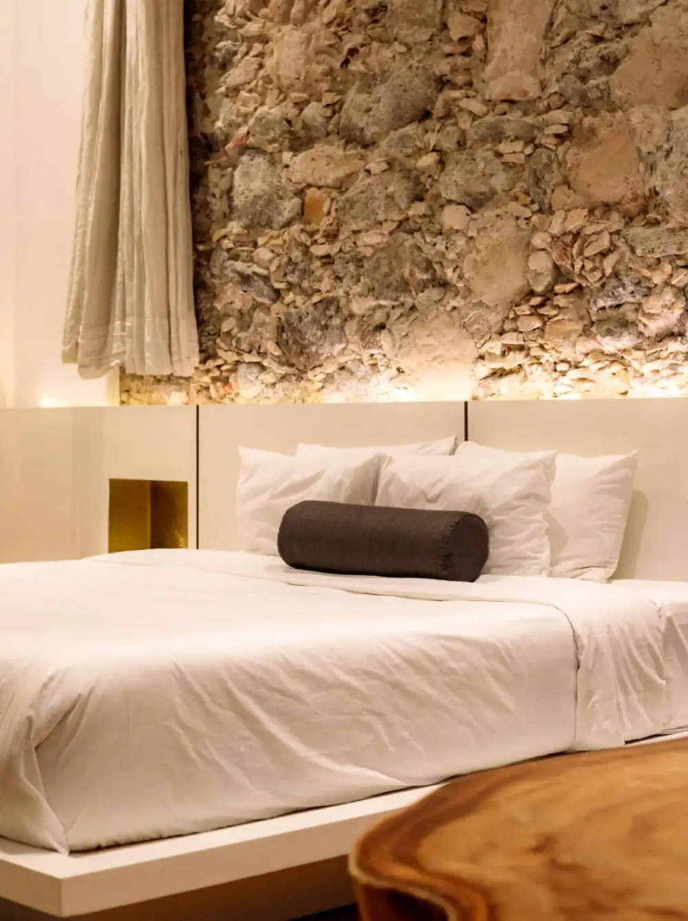 Detalle de cama con ropa blanca y muro de piedra original del Mesón Santa Rosa