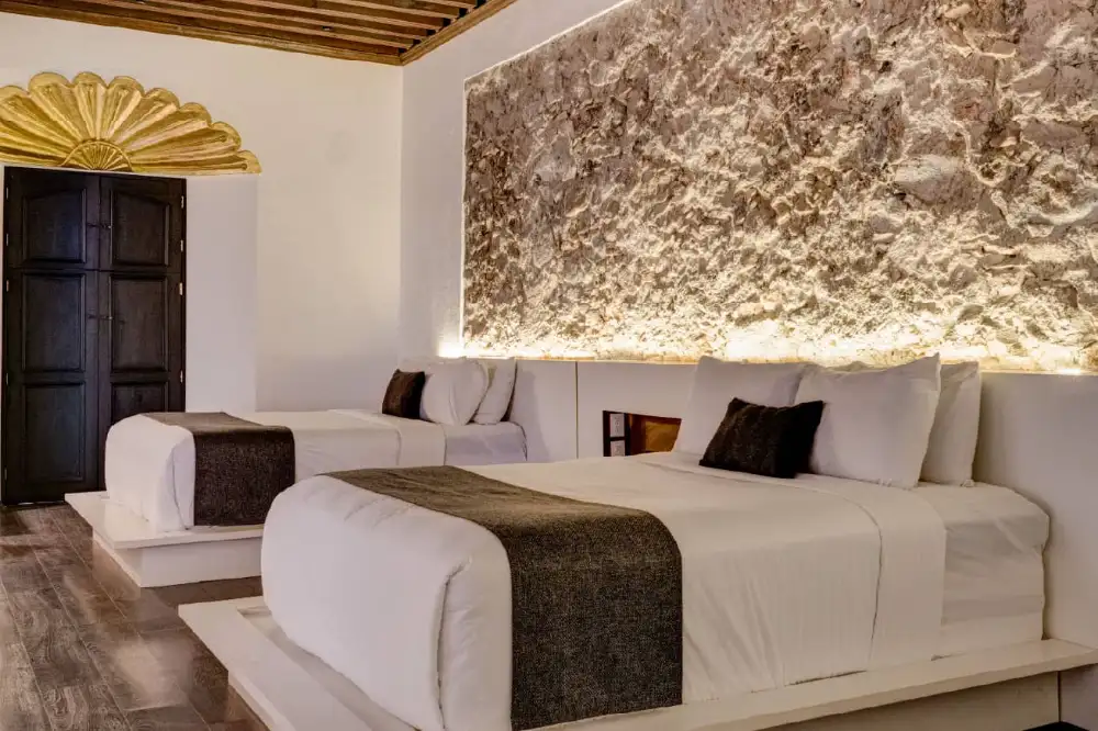 Habitación con muro de piedra iluminado y dos camas en el Mesón Santa Rosa