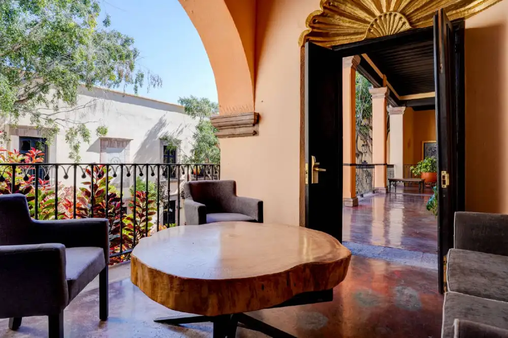 Terraza con mesa de madera y sillones frente a pasillo colonial en el Mesón Santa Rosa, Querétaro