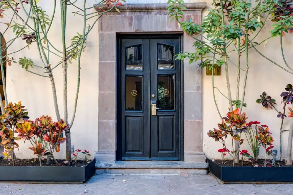 Puerta de acceso de madera oscura entre jardineras en la fachada del Mesón Santa Rosa