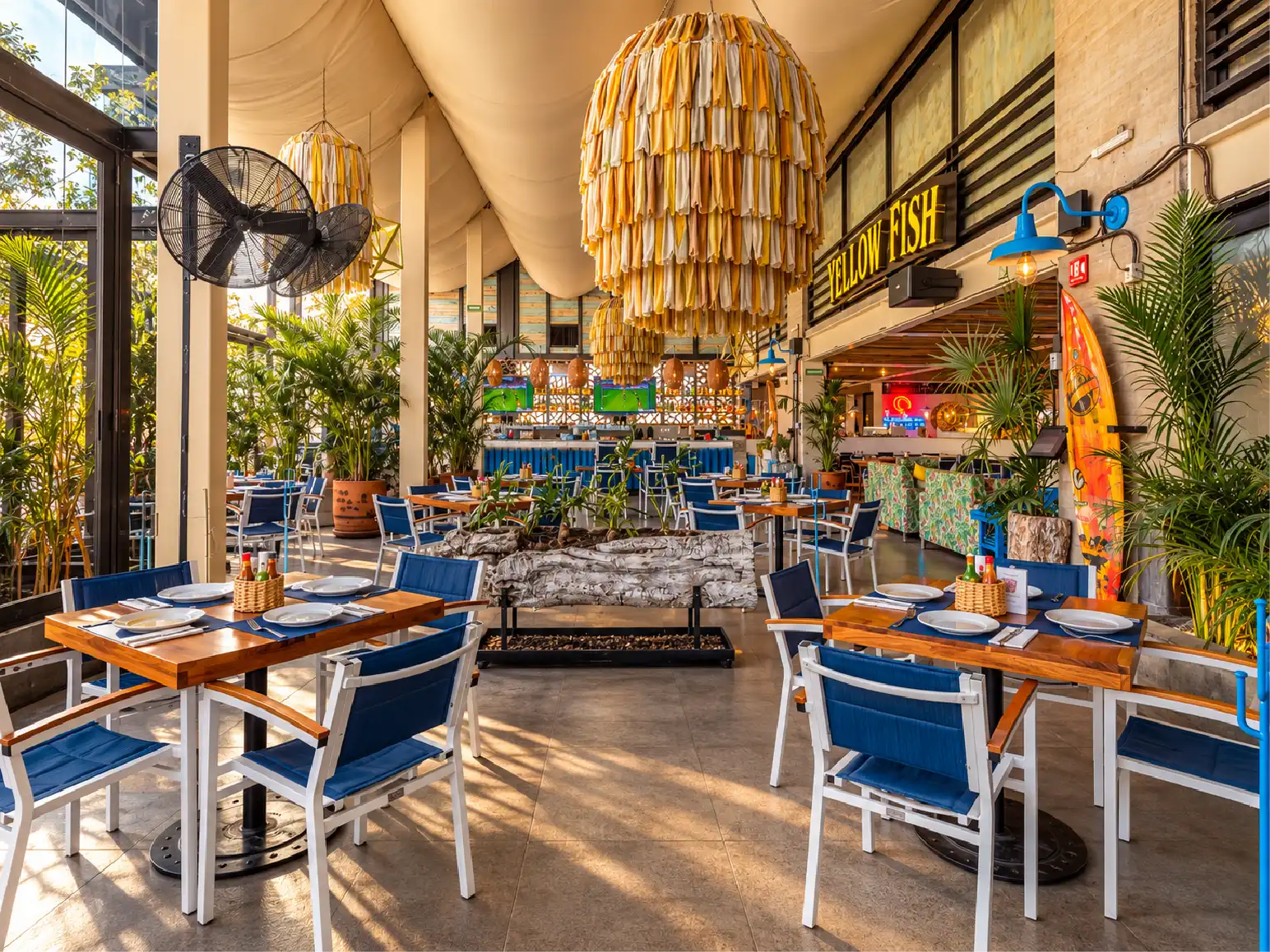 Comedor de doble altura con techo textil, lámparas de fibra y mesas de madera en Yellow Fish Querétaro