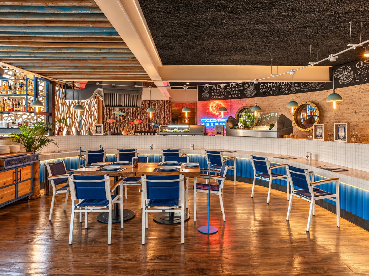 Barra curva con azulejo blanco, iluminación azul y pizarras de menú en el local gastronómico Yellow Fish