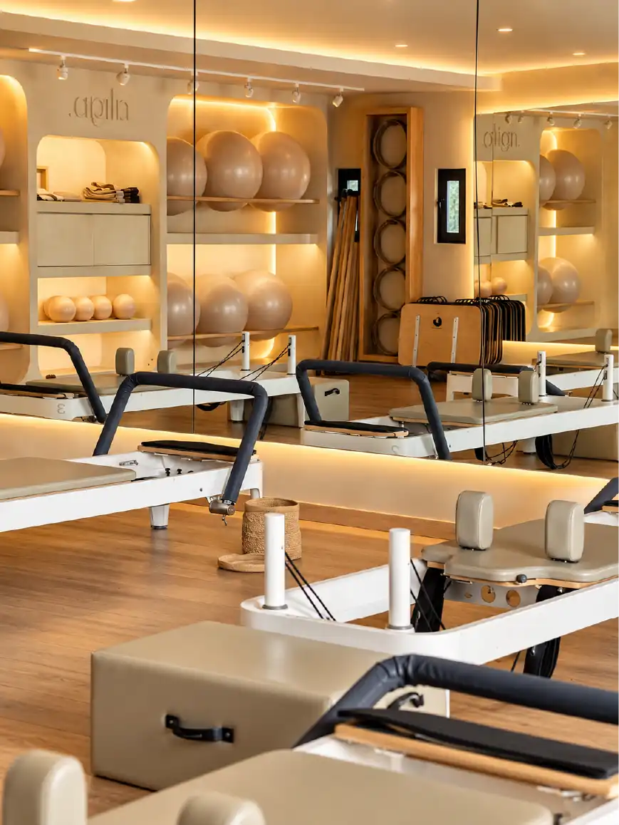 Espejos y nichos con iluminación indirecta reflejando las camas reformer en la remodelación del estudio de pilates Align