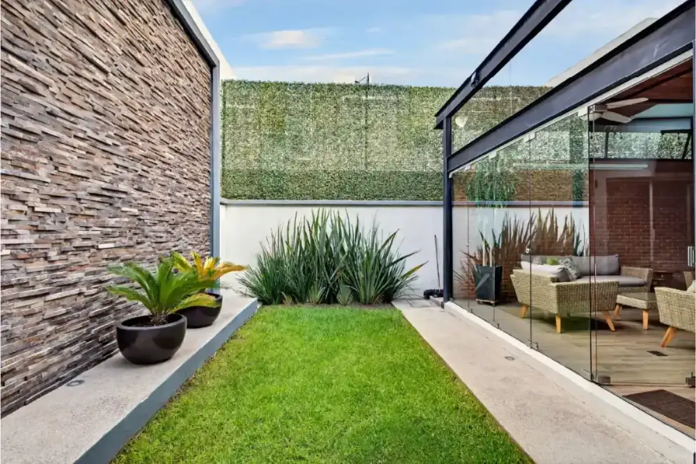 Sala exterior con muro de piedra iluminado, jardín interior y mobiliario tejido de noche