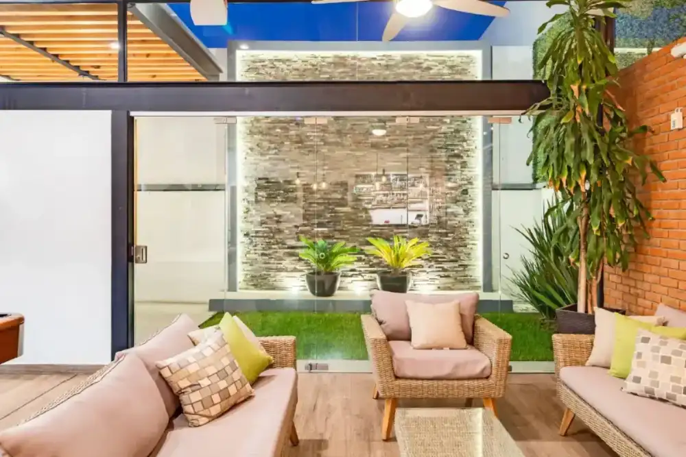 Jardín trasero con muro de piedra laja, pasto y acceso de cristal a la terraza cubierta