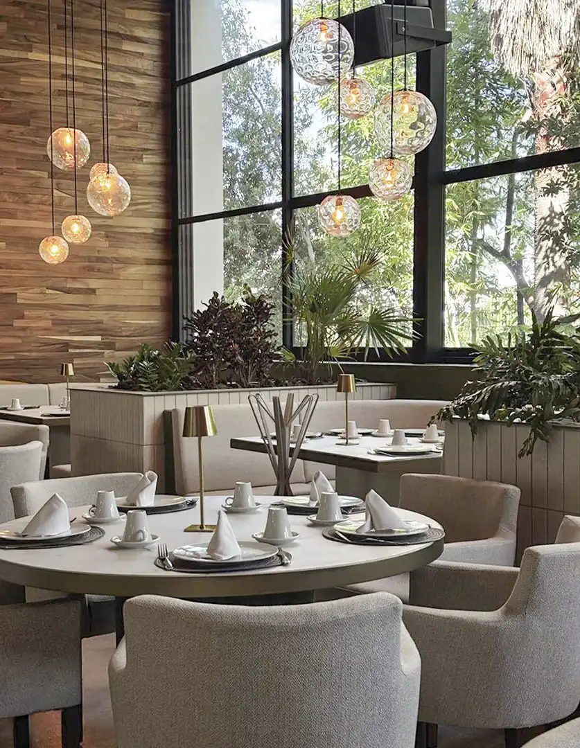 Mesa redonda con lámparas de vidrio y ventanales hacia el jardín en restaurante de Querétaro